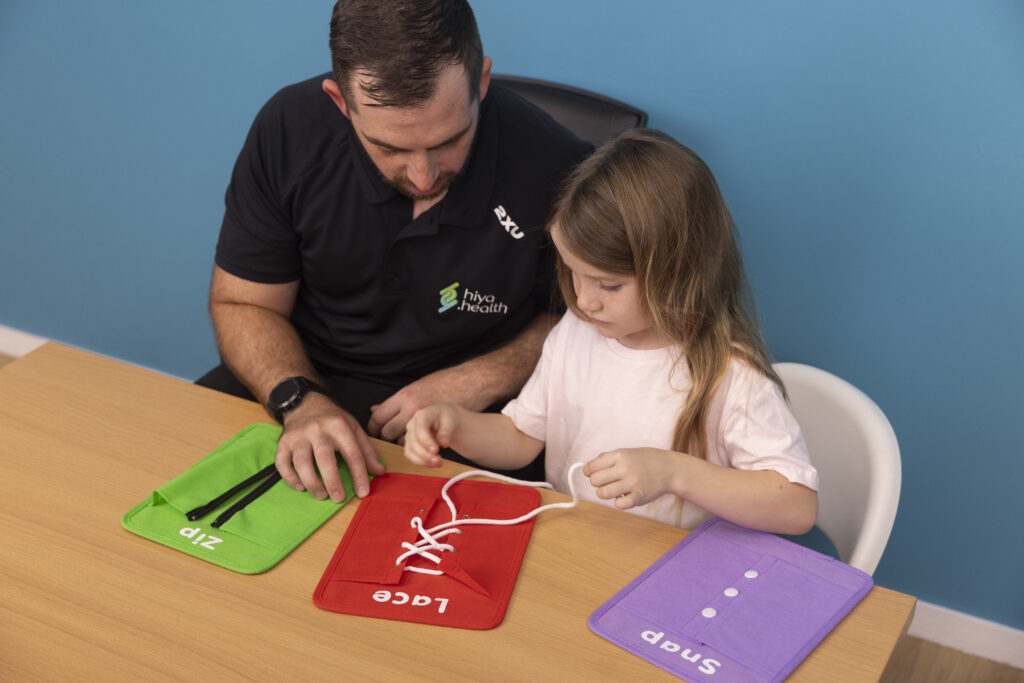 Occupational therapist with young NDIS client learning to tie shoelaces